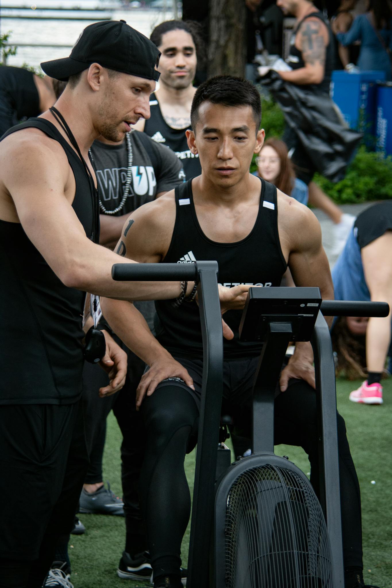 Asian man on stationary bike during an outdoor fitness session with a trainer.