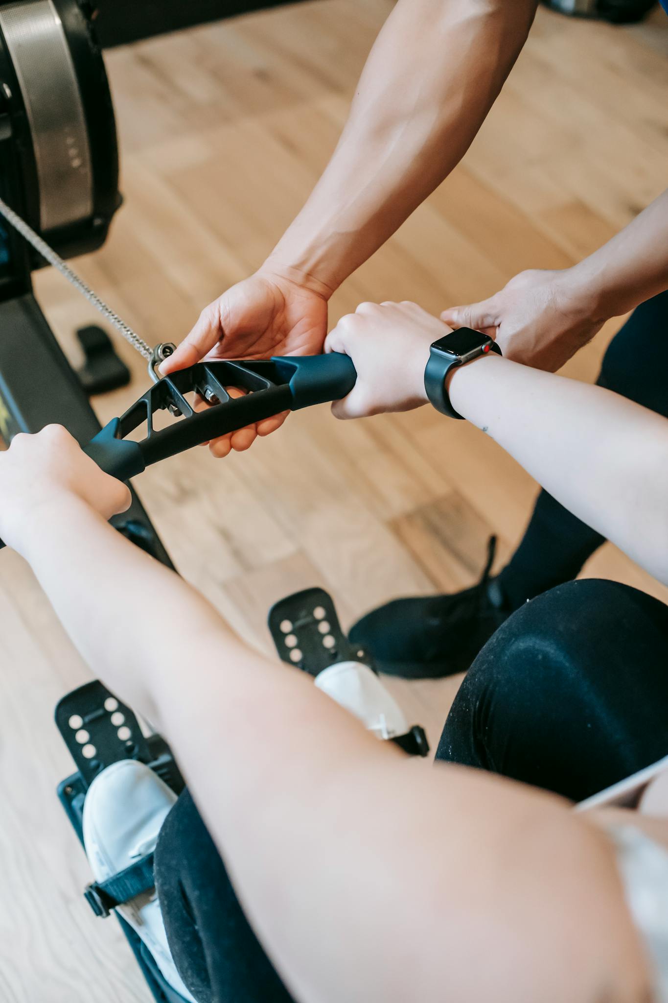 High angle of crop anonymous trainer assisting woman exercising on rowing machine in sports club