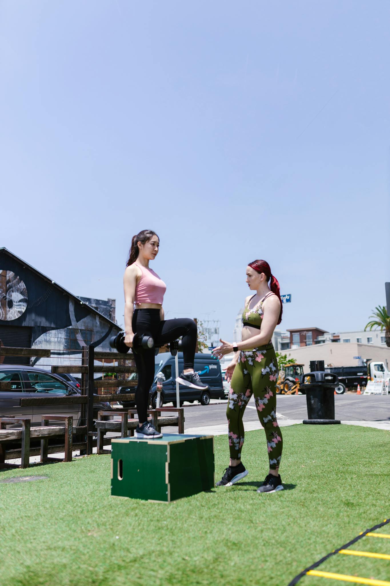 Two women engaged in outdoor fitness training, focusing on step-up exercises under clear blue skies.